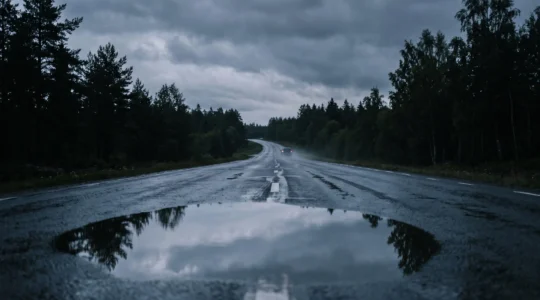 Route mouillée au crépuscule avec un reflet du ciel dans une flaque annonçant un danger de glisse imminent