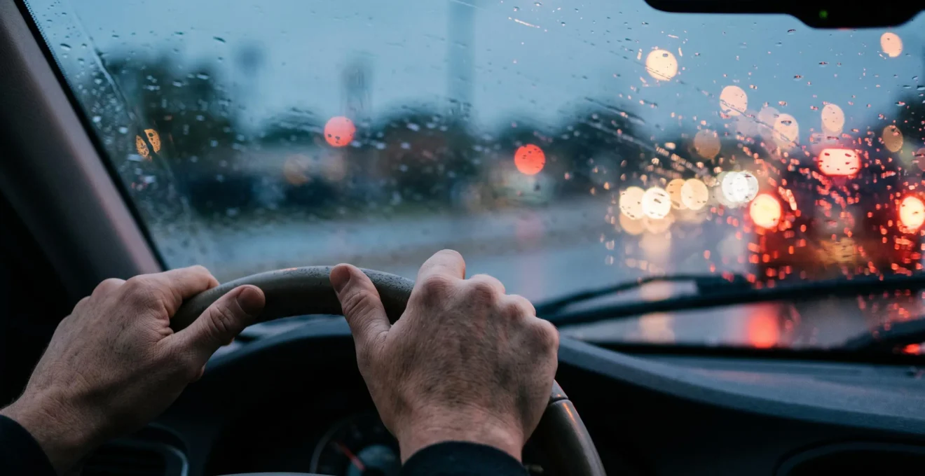 Vue rapprochée d'un conducteur tendu au volant sous la pluie, symbolisant les instants critiques où le risque d'accident augmente fortement
