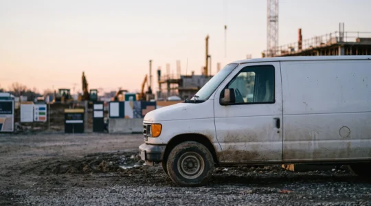 Utilitaire robuste garé en bordure d'un chantier BTP boueux au petit matin, symbole de fiabilité mécanique sur dix ans